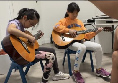 Two students playing guitar together in a classroom.
