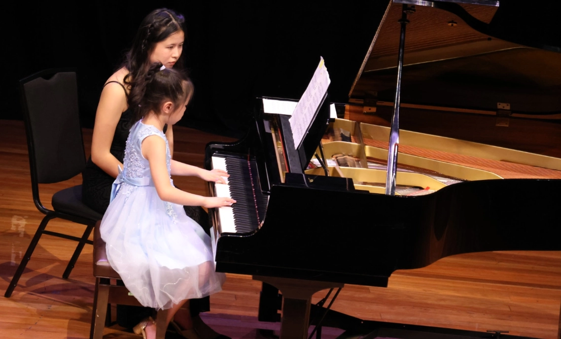 music_kids A student playing piano next to the teacher.